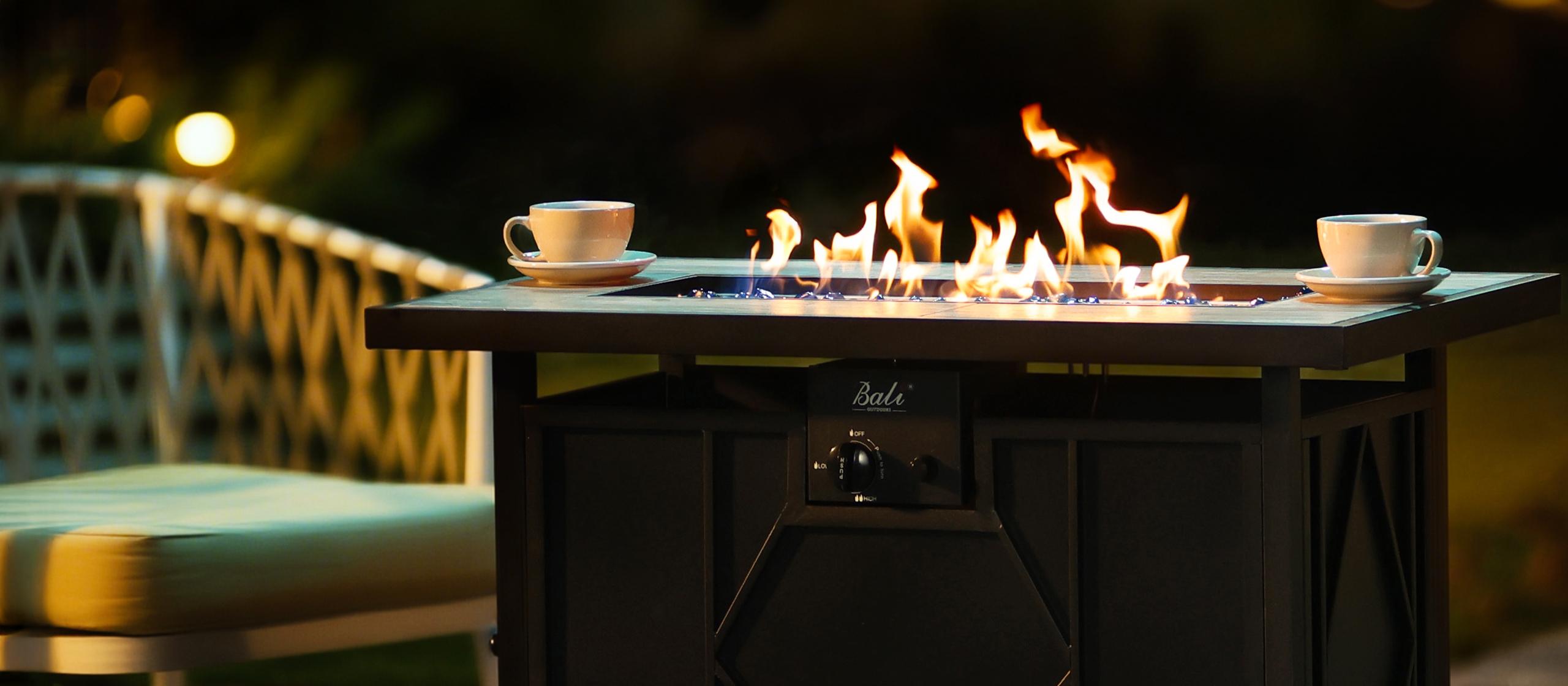 Black metal outdoor fire pit table with two coffee cups and glowing flames.