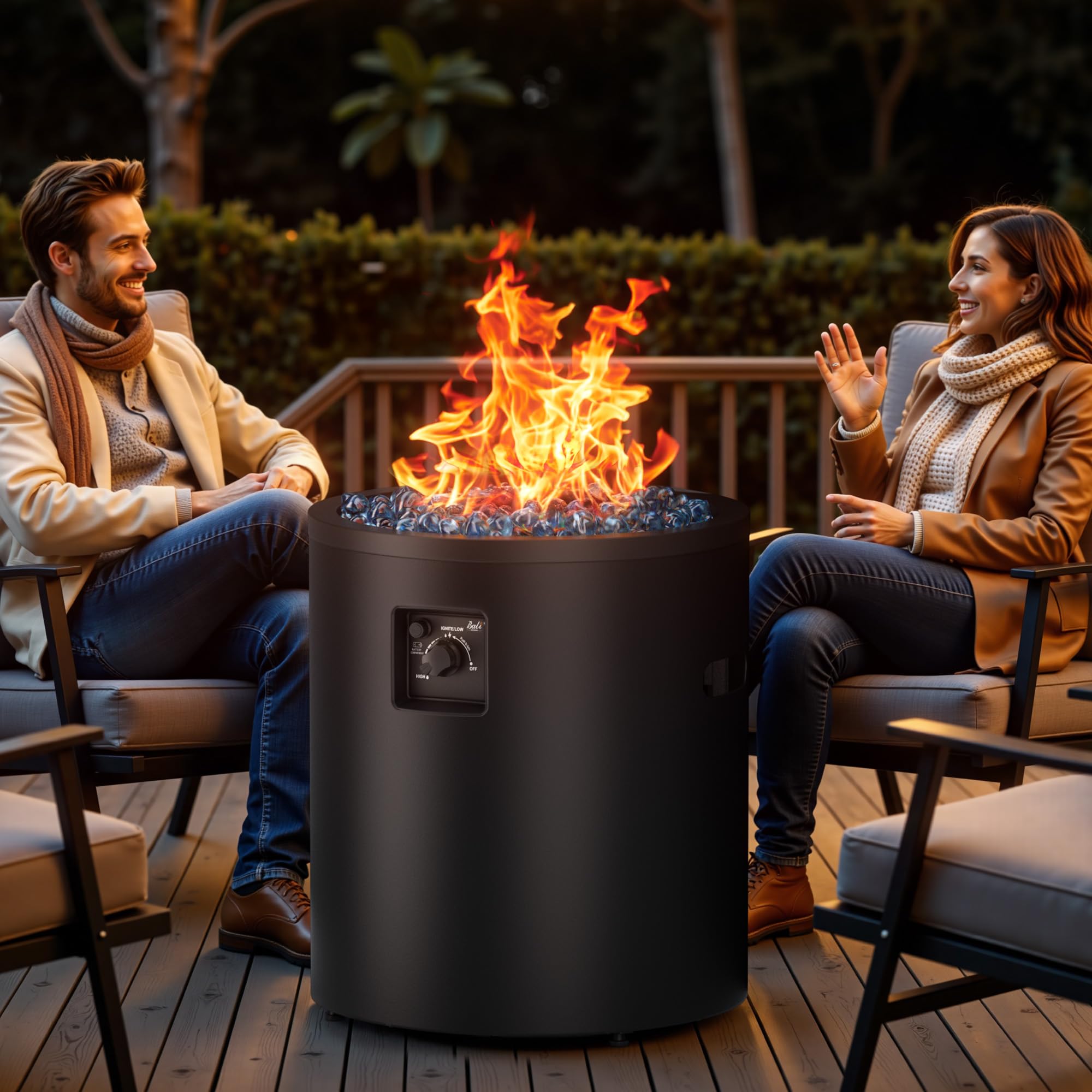 Black 23 inch propane fire pit with blue fire glass on a deck with a couple enjoying the flames.