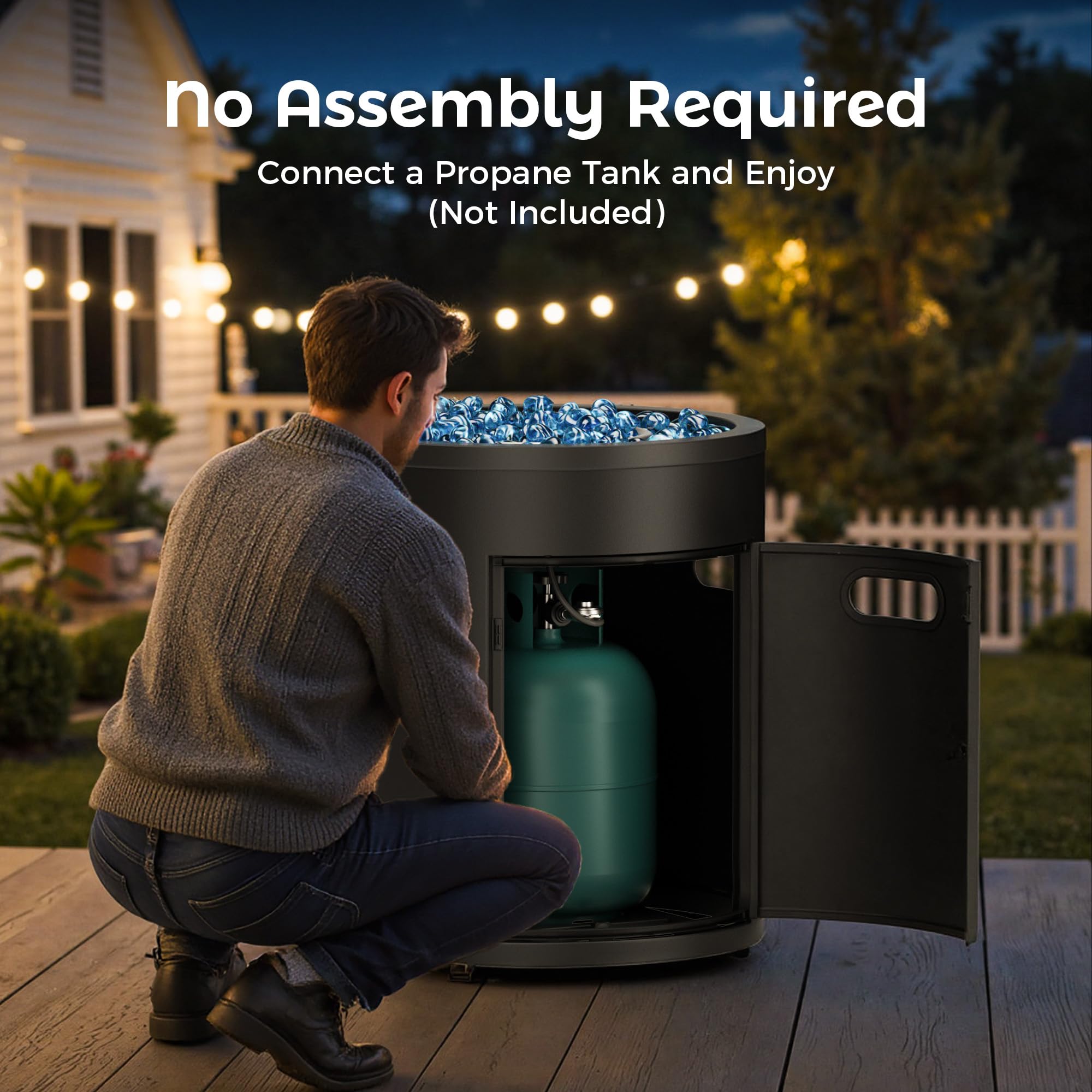Man connecting propane tank to black 23 inch fire pit with blue fire glass on deck at dusk.