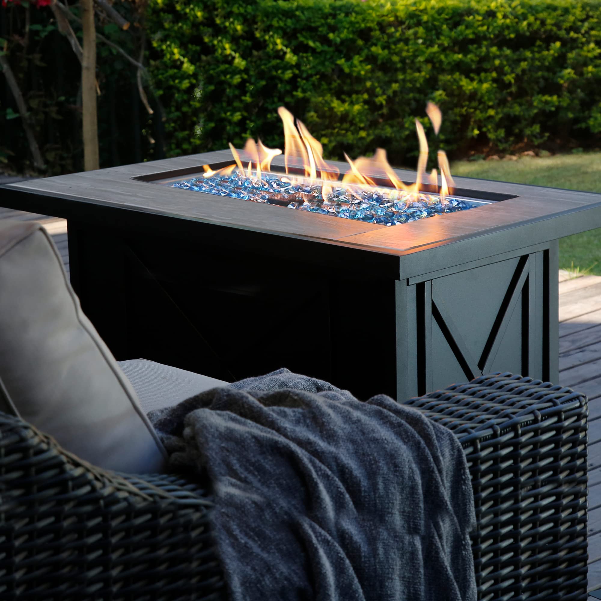 42 inch propane fire pit table with ceramic top, black base, blue glass stones and dancing flames in backyard.