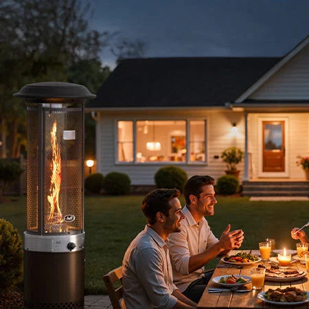 A group of friends enjoy an evening dinner party in a backyard, gathered around a table next to a tall flame patio heater