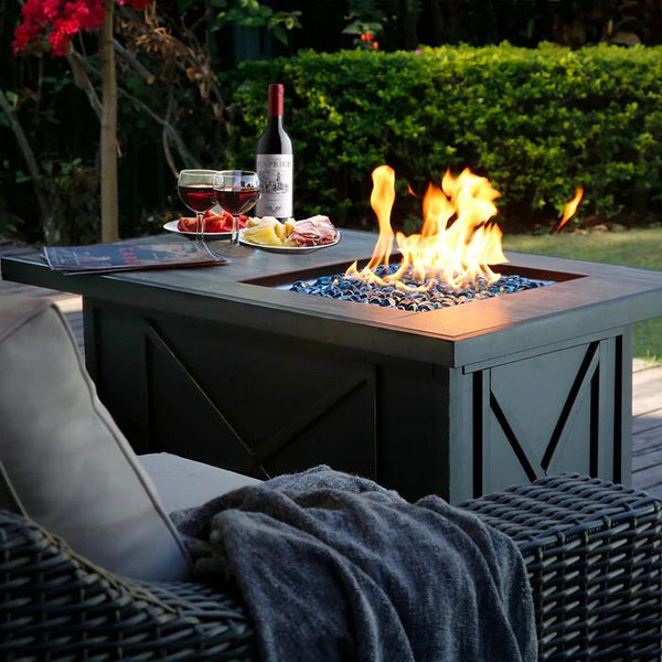 Outdoor fire pit table with blue glass rocks, burning flame, wine, and food on a patio deck